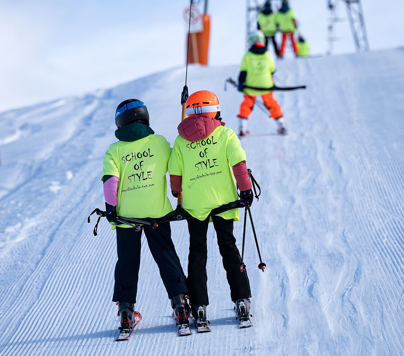 Zwei Kinder mit gleber Weste benutzen den Schlepplift