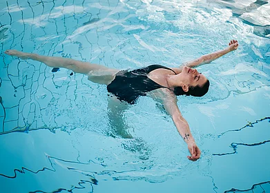 Frau treibt entspannt auf dem Rücken im Pool, Augen geschlossen, Arme ausgestreckt