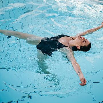 Frau treibt entspannt auf dem Rücken im Pool, Augen geschlossen, Arme ausgestreckt