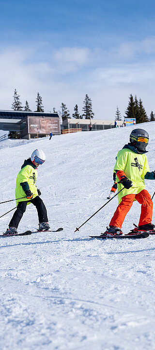 Mehrere Kinder mit gelber Weste fahren auf der Piste. 
