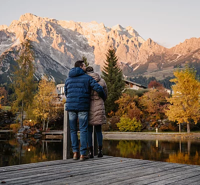 romantik-uebergossene-alm-resort-salzburg-012 Mann und Frau umarmen sich vor der Naturkulisse Hochkönig und Almsee im Herbst