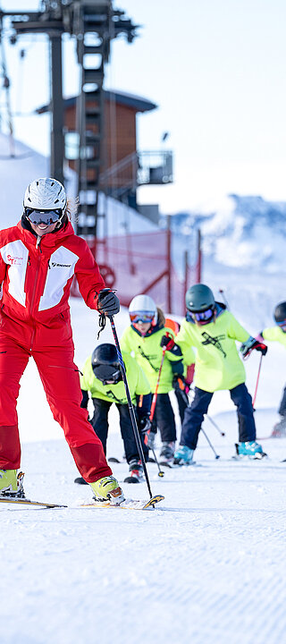 Mehrere Kinder mit gelber Weste folgen dem Skilehrer auf der Piste