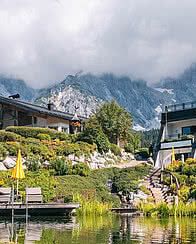 Blick über den hoteleigenen Almsee auf das Wellnesshotel und die dahinterliegende Bergwelt